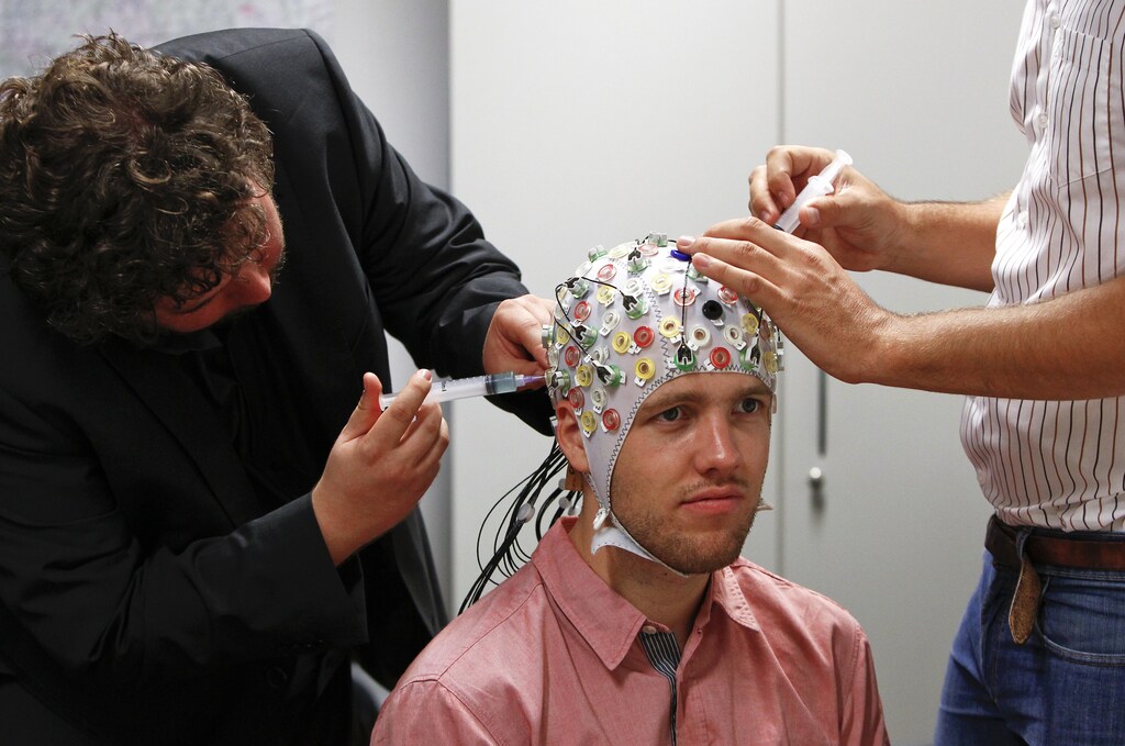 Researchers Thorsten Zander (L) and Jonas Broenstrup inject gel under the electroencephalography (EEG) cap on test person Niklas Thiel at the Technische Universitaet Muenchen (TUM) in Garching near Munich September 9, 2014. The researchers from TUM and the Technische Universitaet Berlin (team Phypa) try to find ways to control an airplane with computer translated brain impulses without the pilot touching the plane's controls. The solution, if achieved, would contribute to greater flight safety and reduce pilots' workload. Picture taken September 9, 2014. REUTERS/Michaela Rehle (GERMANY - Tags: HEADSHOT SOCIETY SCIENCE TECHNOLOGY) - RTR45SH2