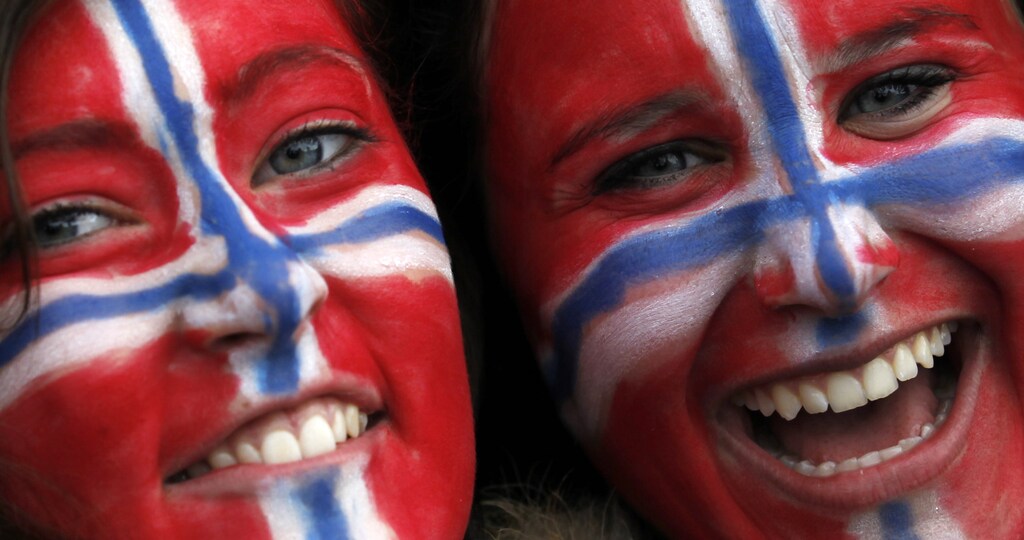 two women with the norwegian flag painted on their face smile for a photograph