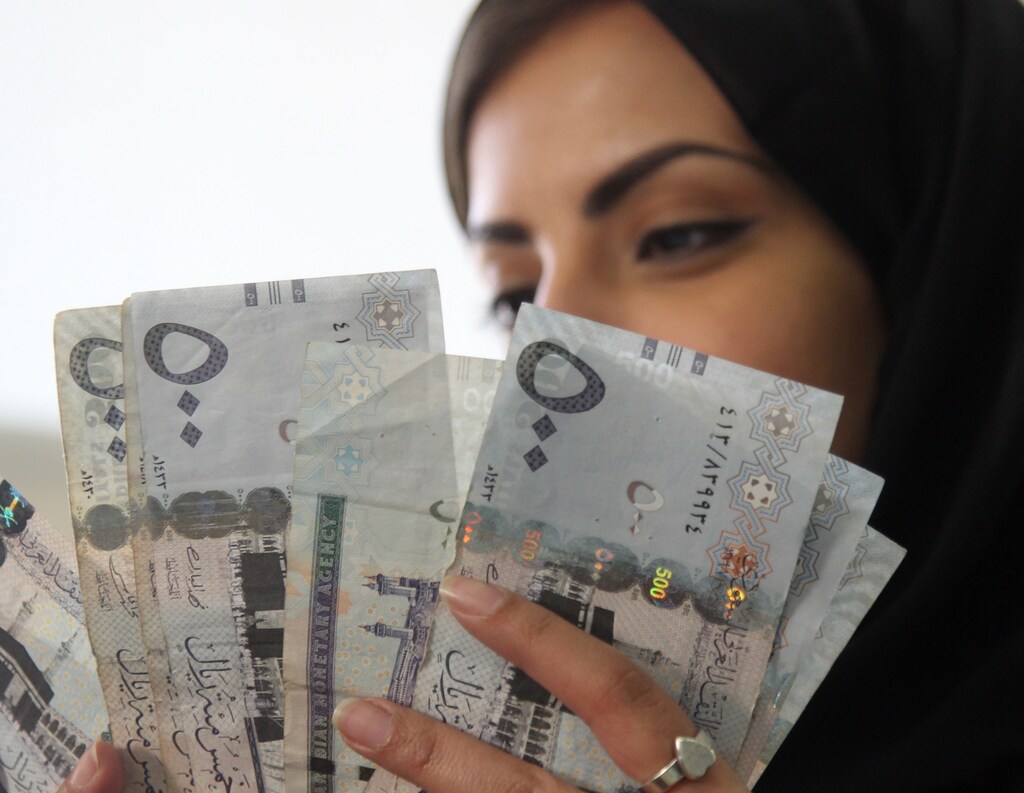 A Saudi woman poses with Saudi riyal banknotes at a money exchange shop in Riyadh, Saudi Arabia January 20, 2016. REUTERS/Faisal Al Nasser - RTX237Q3