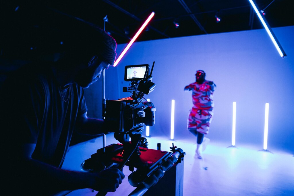 A man holding a camera filming a person in a studio.