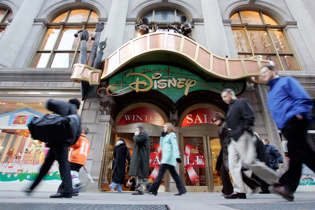 Passers-by walk in front of the World of Disney store in New York January 19, 2006. Walt Disney Co. is in serious talks about an acquisition of Pixar Animation Studios, the Wall Street Journal reported on Thursday, citing people familiar with the matter. REUTERS/Keith Bedford - RTR18GN5