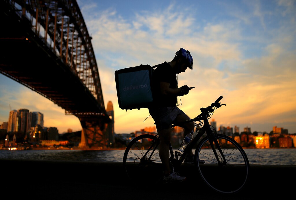 A delivery man checks his phone as he rests on his bicycle under the Sydney Harbour Bridge at sunset in Sydney, Australia October 26, 2016.