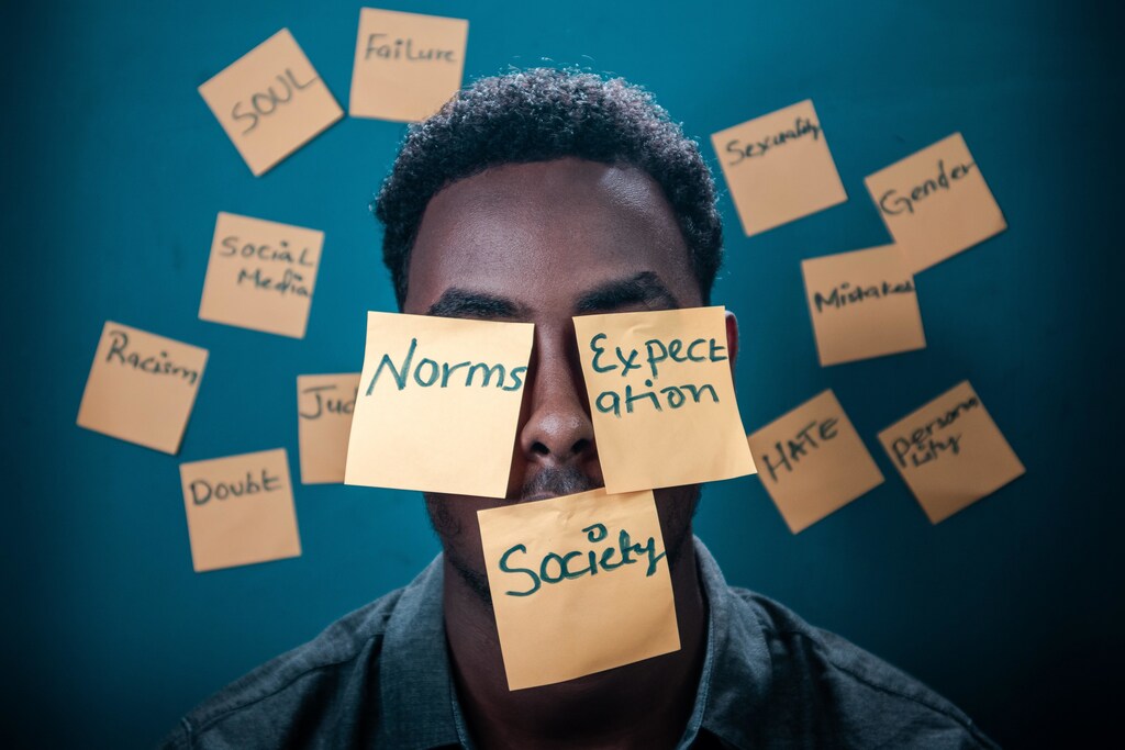 A man surrounded by post-its with 'norms', 'expectation' and 'society' written on them