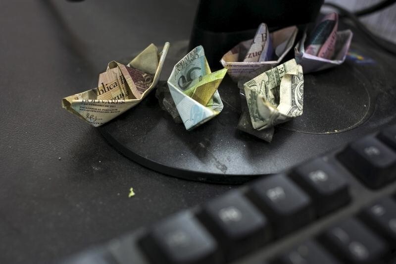 Venezuelan bolivar banknotes and a U.S. dollar banknote, folded as boats, are seen at a fruit and vegetable store in Caracas July 10, 2015. Origami-like boats made from Venezuela's rapidly depreciating bolivar bills sit on the cash register of the small fruit and vegetable store in Caracas. Cashier Marisol Garcia makes the bolivar boats to illustrate roaring inflation and the currency's tumble on the black market, where even the country's biggest bill is worth just 16 U.S. cents.