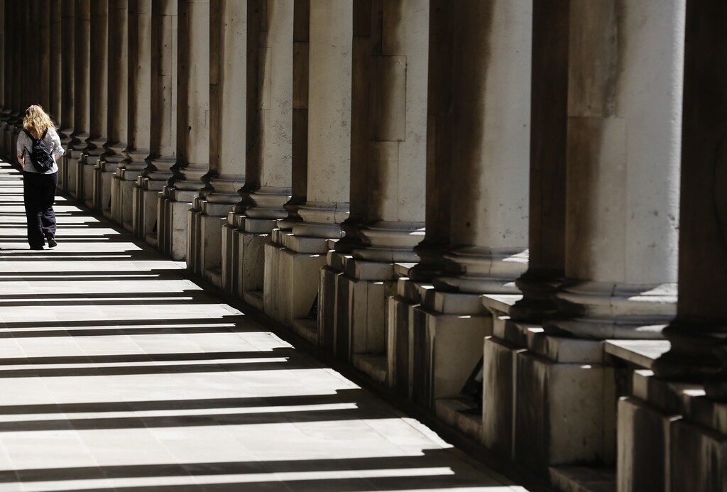 A woman walks through shadows cast by columns at the Old Royal Naval College in Greenwich east London June 10, 2014.