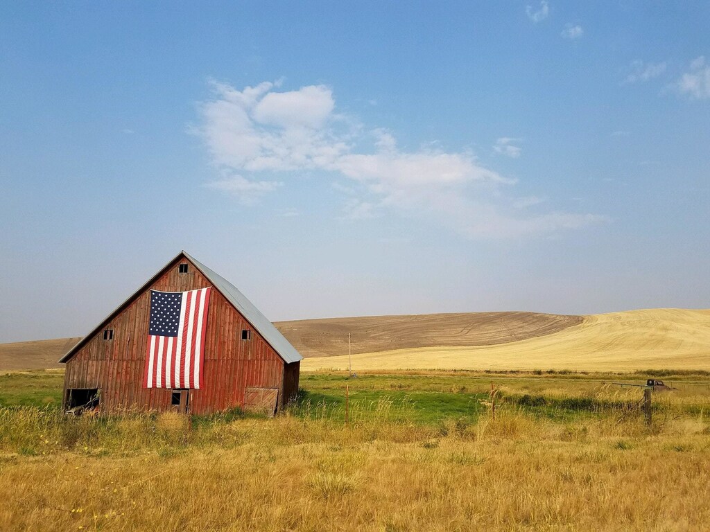 a barn with an american flag on the exterior, in a remote, agricultural landscape