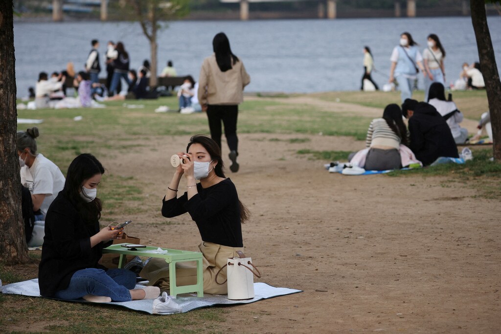 A woman wearing a mask and putting on make-up in a park in Seoul, South Korea.
