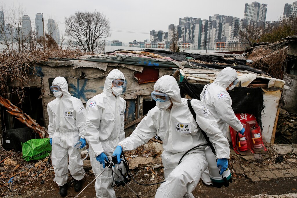 South Korean soldiers in protective gears sanitize shacks as a luxury high-rise apartment complex is seen in the background at Guryong village in Seoul, South Korea, March 3, 2020.
