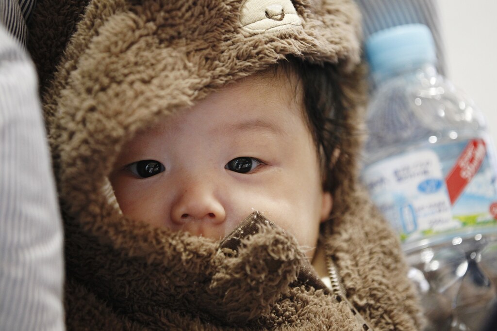 A baby lies in a carriage as his mother receives bottled water at a ward office in Tokyo, March 24, 2011. Stores in Tokyo were running out of bottled water on Thursday after radiation from a damaged nuclear complex briefly made tap water unsafe for babies, while more nations curbed imports of Japanese food. Engineers are trying to stabilise a six-reactor nuclear plant in Fukushima, 250 km (150 miles) north of the capital, nearly two weeks after an earthquake and tsunami battered the plant and devastated northeast Japan, leaving nearly 26,000 people dead or missing. REUTERS/Lee Jae-Won (JAPAN - Tags: DISASTER ENVIRONMENT BUSINESS) - GM1E73O1G4N01