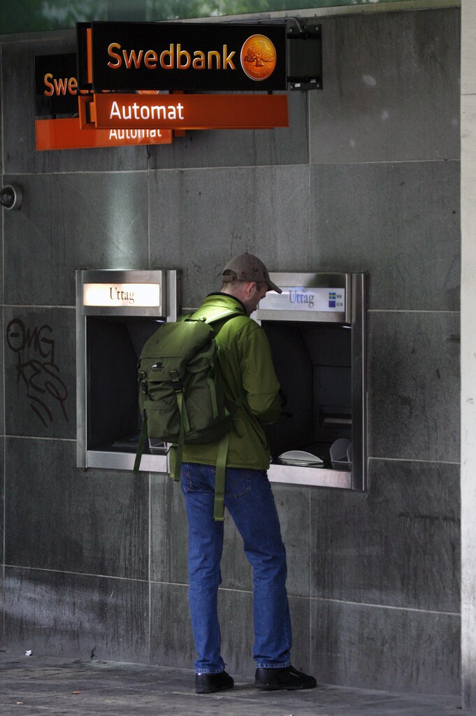 A customer withdraws money from a SwedBank cash machine in downtown Stockholm June 4, 2009. Fresh worries that Latvia, mired deep in recession, might have to devalue its currency have weighed on the stocks of some of Sweden's top banks over the past few days due to the billions of crowns worth of loans the banks have extended in the region. REUTERS/Bob Strong (SWEDEN BUSINESS) - GM1E5641TAM01