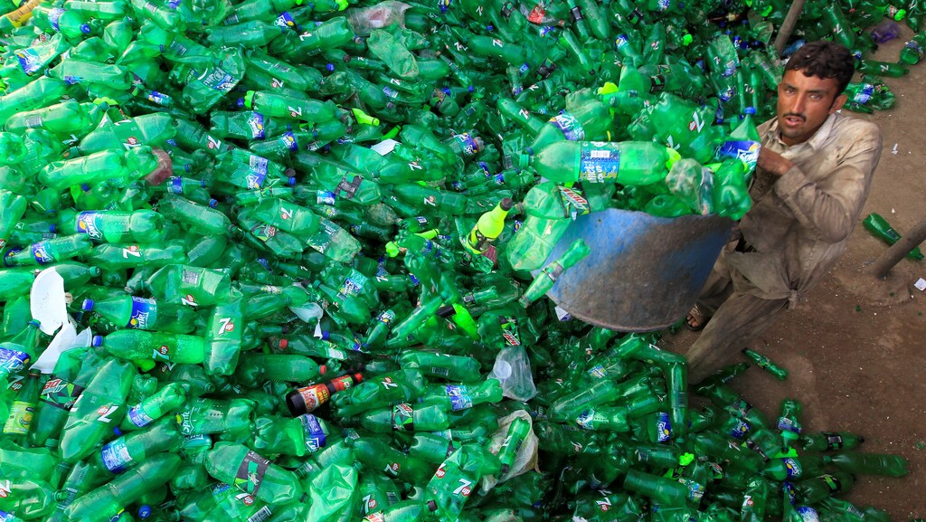 A worker picks up bottles to throw in a plastic bottle chipper at a recycling workshop in Pakistan