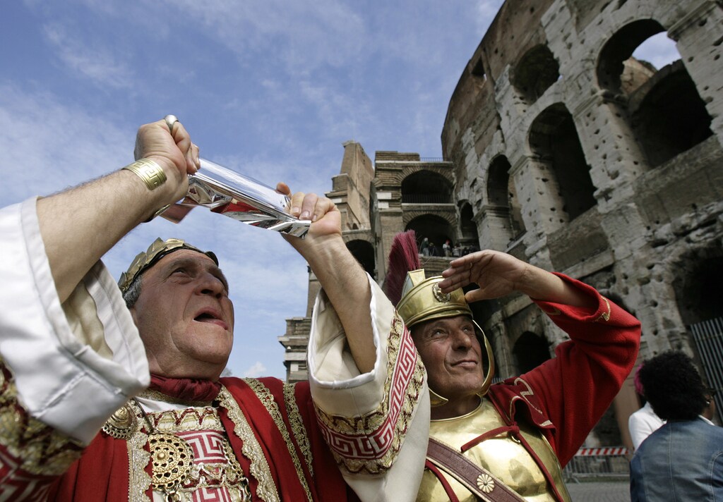 A pair of Italian men dressed as a former Roman emperor and gladiator, who make their living posing with tourists, use a special filter to view a partial eclipse of the sun outside the Colosseum in Rome March 29, 2006. REUTERS/Chris Helgren - GM1DSGPXDHAA
