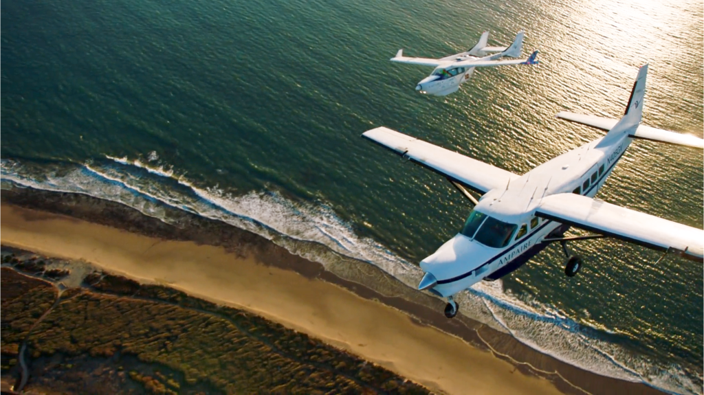 Imagen aérea de dos aviones híbridos sobrevolando el mar y una playa.