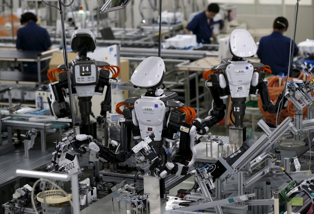 Humanoid robots work side by side with employees in the assembly line at a factory of Glory Ltd., a manufacturer of automatic change dispensers, in Kazo, north of Tokyo, Japan, July 1, 2015. Japanese firms are ramping up spending on robotics and automation, responding at last to premier Shinzo Abe's efforts to stimulate the economy and end two decades of stagnation and deflation. Picture taken July 1, 2015. REUTERS/Issei Kato - GF10000147190