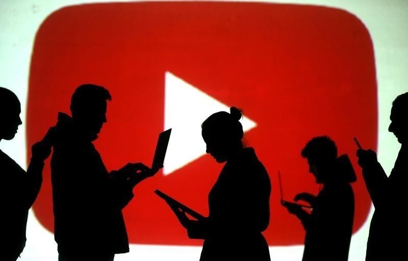 Silhouettes of laptop and mobile device users are seen next to a screen projection of Youtube logo in this picture illustration taken March 28, 2018.