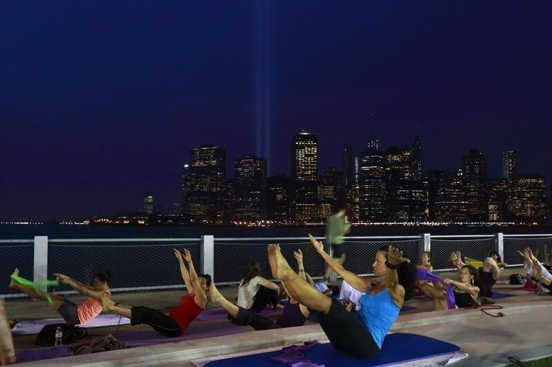 Instructor Lou Cornacchia (C) leads a pilates class on Pier 5 at Brooklyn Bridge Park as the Tribute in Lights illuminates the sky over Lower Manhattan on the 12th anniversary of the 9/11 attacks in New York September 11, 2013. Bagpipes, tolling bells and a reading of the names of the nearly 3,000 people who died when hijacked jetliners crashed into the World Trade Center, the Pentagon, and a Pennsylvania field marked the 12th anniversary of the September 11 attacks in 2001. REUTERS/Brendan McDermid (UNITED STATES - Tags: DISASTER ANNIVERSARY CITYSCAPE) - GM1E99C0QDW01