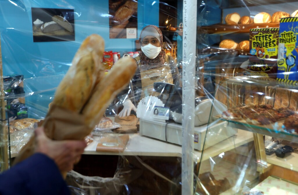 Un residente sostiene baguettes francesas después de haberlas metido por un agujero en una protección de plástico en una panadería en Fontenay-sous-Bois cerca de París durante el brote de la enfermedad del Coronavirus (COVID-19) en Francia, el 15 de abril de 2020.