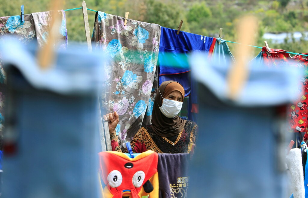 Una mujer refugiada siria que lleva una máscara facial cuelga la ropa para que se seque, mientras el Líbano extiende un encierro de dos semanas para combatir la propagación de la enfermedad coronavirus (COVID-19) en un campamento de refugiados sirios en la aldea de Ketermaya, Líbano 26 de marzo de 2020.