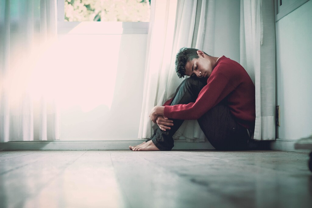 A man sat in a corner hugging his knees to his chest