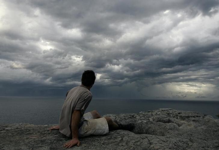 A man watches seasonal autumn storm clouds gather over the sea ahead of steady rain off the coast of Sydney March 8, 2007. Many parts of Australia are in the grip of the worst drought in 100 years, forcing authorities to impose water restrictions exacerbated when rainfall misses catchment areas. REUTERS/Will Burgess (AUSTRALIA)