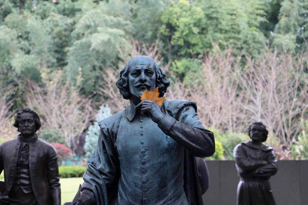 A statue of William Shakespeare in a park.