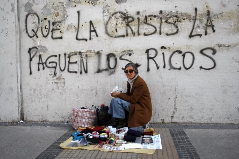 A street vendor sits in front a wall that reads "That the crisis pay the rich", in downtown Santiago June 7, 2009. REUTERS/Ivan Alvarado (CHILE BUSINESS SOCIETY EMPLOYMENT) - GM1E5671TFU01
