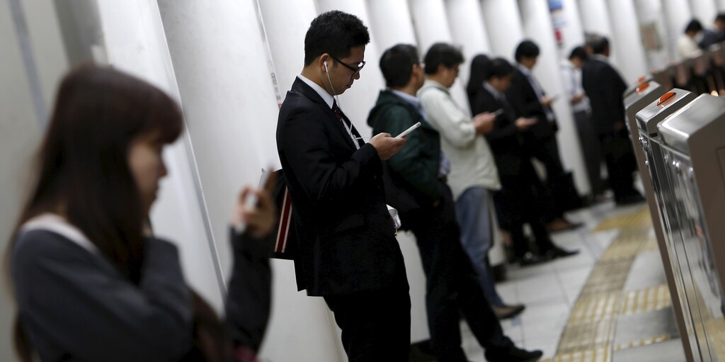 People look at their mobile phones while waiting for a train at a subway station in Tokyo, Japan, October 14, 2015.