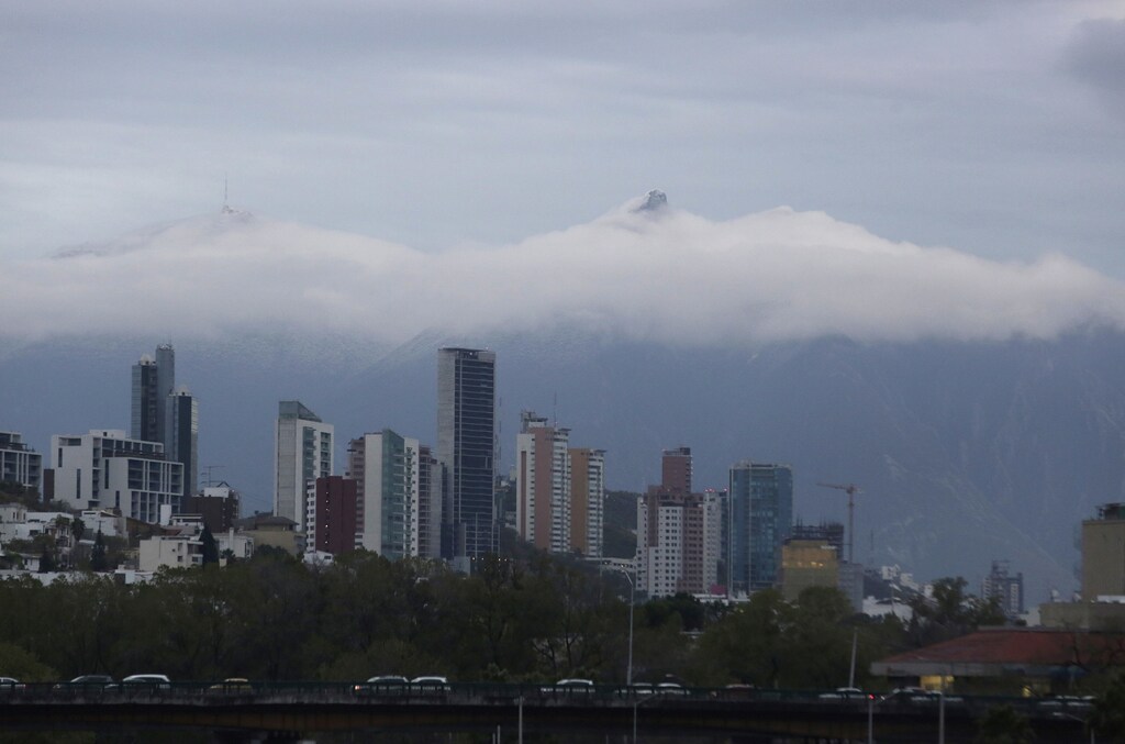 The Cerro de la Silla mountain is seen in the background during cloud cover over Monterrey skyline after a rare snow storm fell in early hours on the outskirts of Monterrey, Mexico, January 27, 2016. REUTERS/Daniel Becerril - RTX24BLV