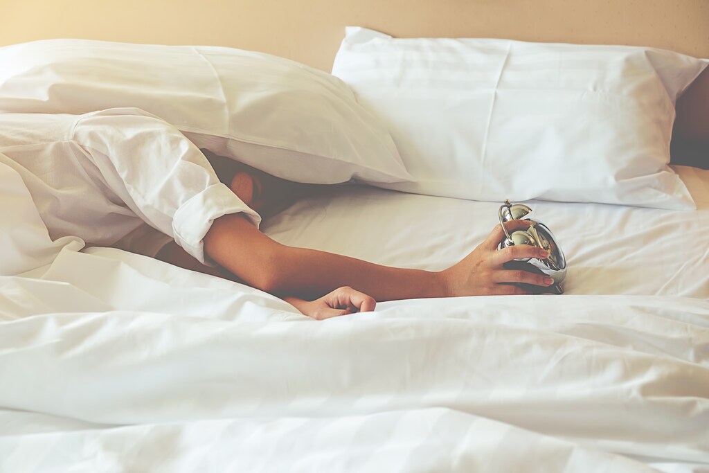 Irritated young woman putting her alarm clock off in the morning with soft morning light. Relaxing concept.