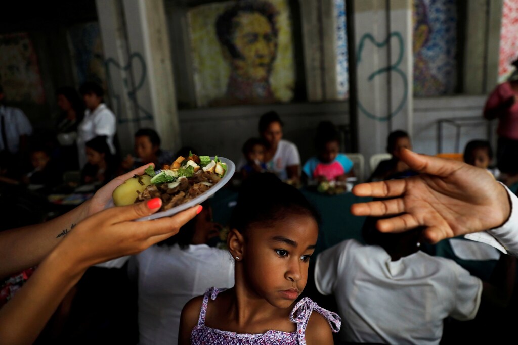 A child looks on, as volunteers of Venezuelan presidential candidate Javier Bertucci of the "Esperanza por el Cambio" party, give food plates to women and children as part of the Mothers day celebration, during a campaign rally in Caracas, Venezuela May 13, 2018. REUTERS/Carlos Jasso TPX IMAGES OF THE DAY - RC1F9FA084F0