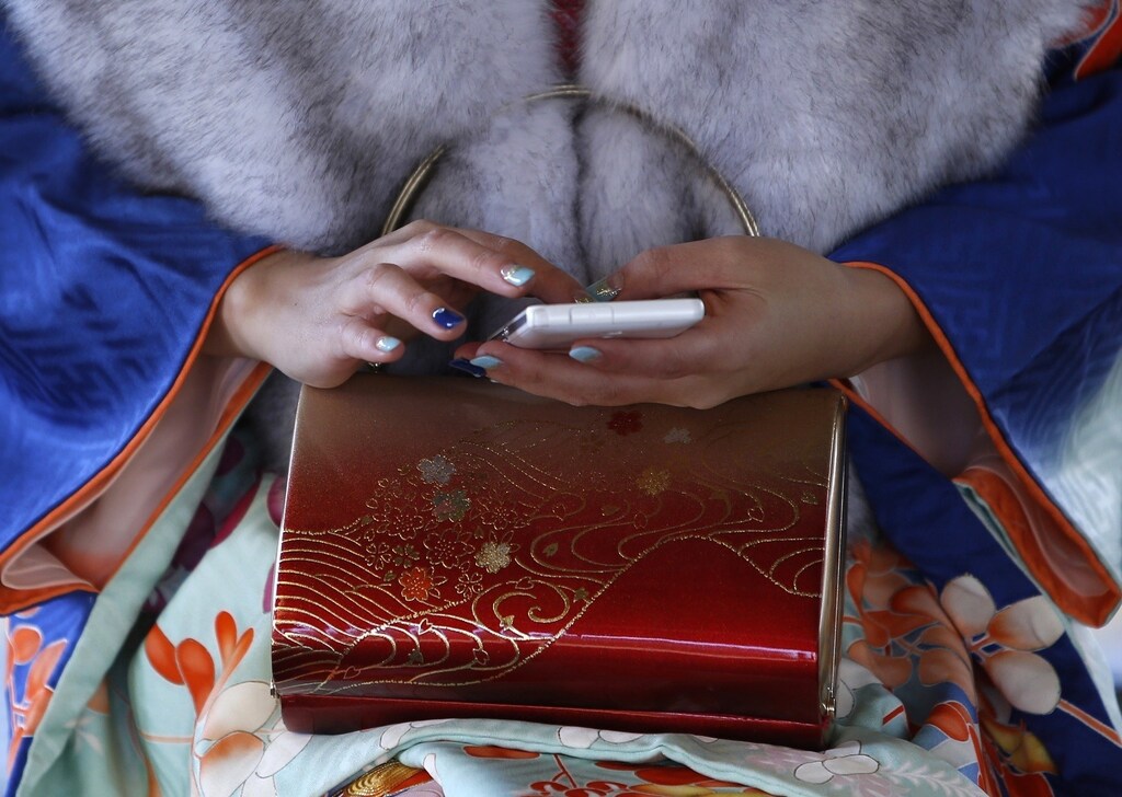 A 20-year-old woman holds her smartphone as she waits for her friends at a train station before a ceremony celebrating Coming of Age Day at an amusement park in Tokyo January 13, 2014. According to a government announcement, about 1,210,000 men and women who were born in 1993 reached coming of age this year and the number is 10,000 less people than last year. The figure is the smallest number since the government started counting in 1968. REUTERS/Yuya Shino (JAPAN - Tags: SOCIETY) - RTX17C6M
