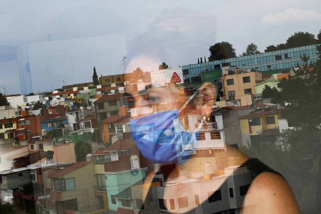 Monica Samudio, 46, whose husband Jorge Garcia, 51, died from the coronavirus disease (COVID-19), is reflected in the window as she looks out of her new apartment, in Mexico City, Mexico April 29, 2020. Samudio said she moved from her previous home after feeling discriminated against when she and her husband contracted the disease. Picture taken April 29, 2020