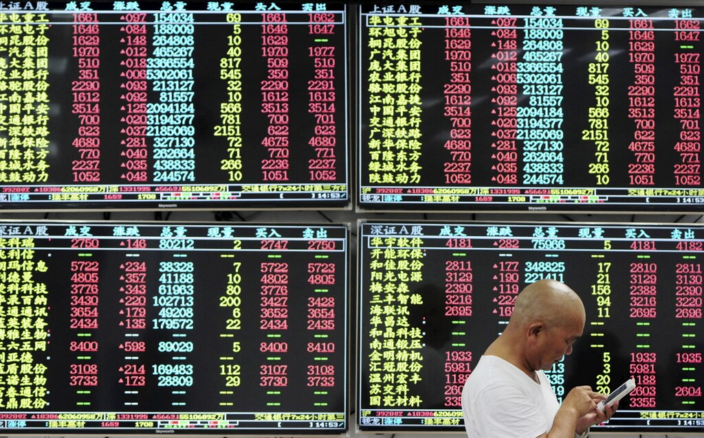 An investor looks at his mobile phone in front of electronic screens showing stock information at a brokerage house in Jiujiang, Jiangxi province, China, August 10, 2015. China stocks jumped more than 4 percent on Monday on possible restructuring among major shipping firms and in other key sectors, and on hopes that less volatile trading may soon convince fund managers to get off the sidelines and re-invest billions in cash