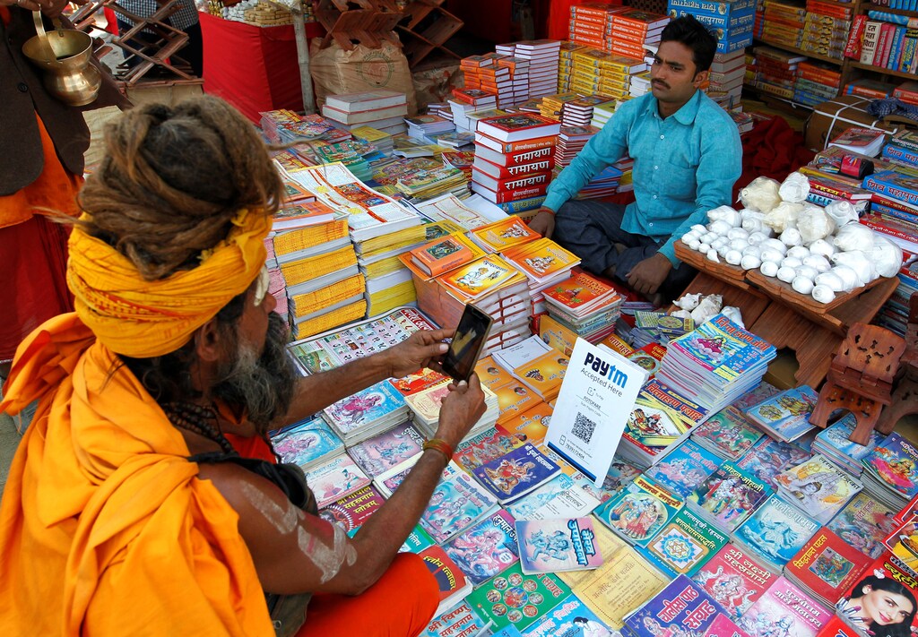 A Sadhu or a Hindu holy man pays the vendor through Paytm, a digital wallet company, after buying a book during the annual religious festival of Magh Mela in Allahabad, India, January 26, 2017. Picture taken January 26, 2017. REUTERS/Jitendra Prakash - RC1559215880