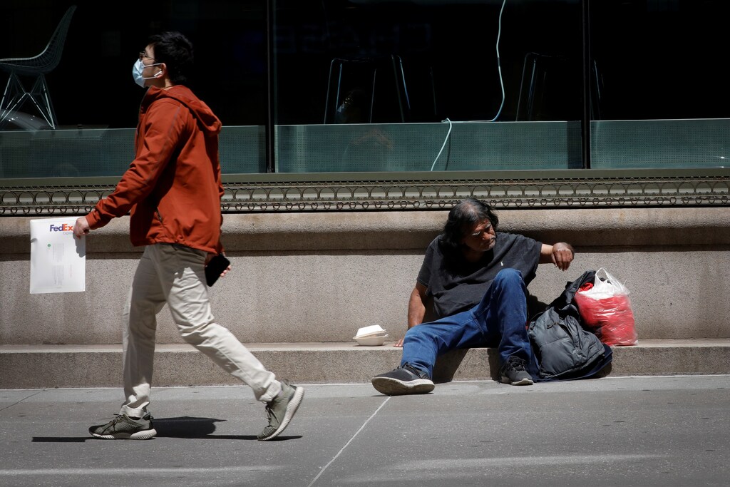A man wearing a protective face mask walks past a homeless man sitting on a sidewalk in Manhattan, during the outbreak of the coronavirus disease (COVID-19) in New York city, New York, U.S., May 5, 2020. REUTERS/Mike Segar - RC2JIG93BO16