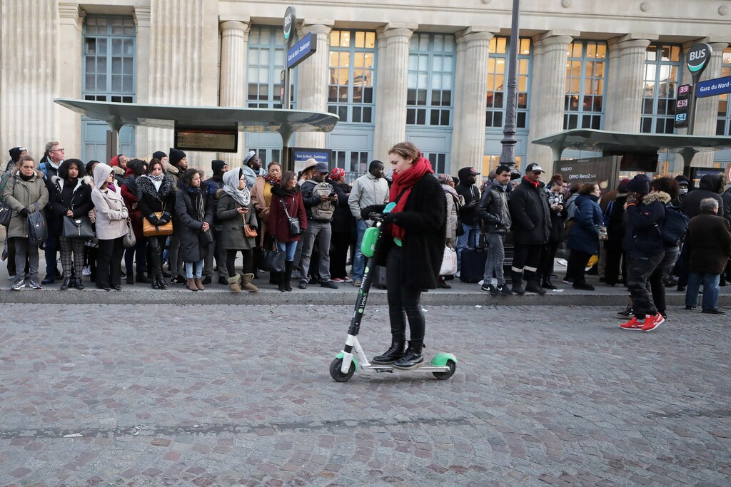 A woman rides a scooter past the people waiting on bus stops at Gare du Nord station during a strike by all unions of the Paris transport network (RATP) and French SNCF workers in Paris as part of a second day of national strike and protests in France, December 10, 2019.