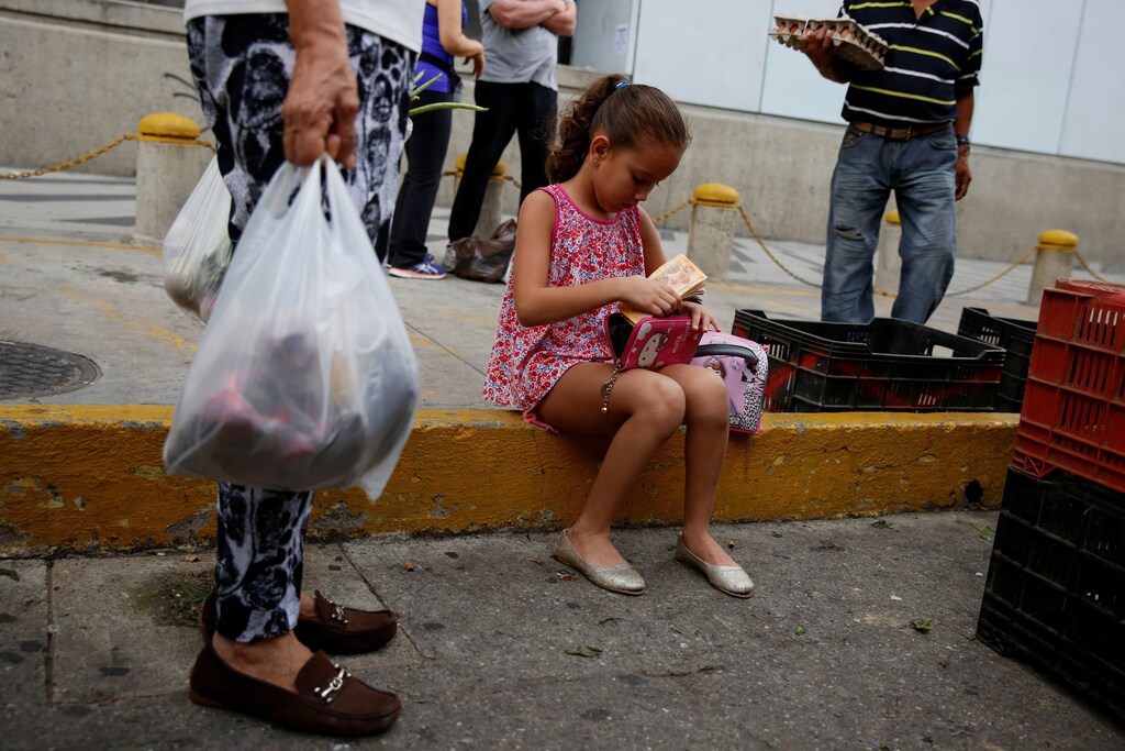 A girl puts Venezuelan bolivar notes into her purse at a street market in Caracas, Venezuela August 13, 2016. REUTERS/Carlos Garcia Rawlins - RTX2KJPT