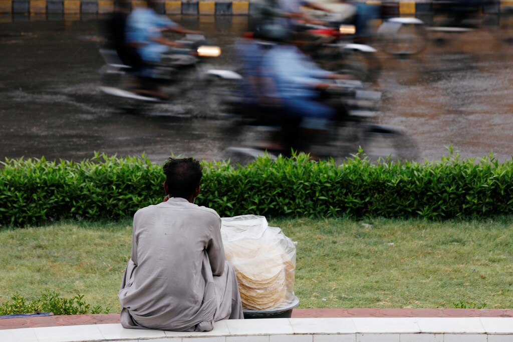Commuters move past a man selling pappadoms as he waits for customers during the monsoon rain, as the coronavirus disease (COVID-19) outbreak continues, in Karachi, Pakistan August 6, 2020. REUTERS/Akhtar Soomro - RC2H8I9PQUEB