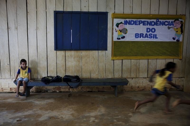 A boy sits as other children run in the corridors of their school in the village of Rio Pardo next to Bom Futuro National Forest, in the district of Porto Velho, Rondonia State, Brazil, August 31, 2015. The banner reads "Independence of Brazil". The town of Rio Pardo, a settlement of about 4,000 people in the Amazon rainforest, rises where only jungle stood less than a quarter of a century ago. Loggers first cleared the forest followed by ranchers and farmers, then small merchants and prospectors. Brazil's government has stated a goal of eliminating illegal deforestation, but enforcing the law in remote corners like Rio Pardo is far from easy. REUTERS/Nacho Doce PICTURE 22 OF 40 FOR WIDER IMAGE STORY "EARTHPRINTS: RIO PARDO" SEARCH"EARTHPRINTS PARDO" FOR ALL IMAGES - GF20000046417