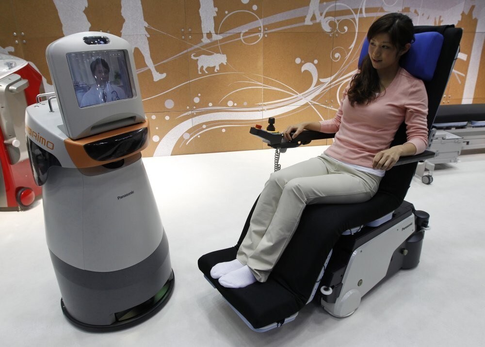 A demonstrator sits in an electronic wheelchair as she talks with a doctor, seen on the monitor of Panasonic's HOSPI-Rimo, at its presentation in Tokyo October 4, 2011. The communications assistant robot, which has automatic movement and visual communication functions, enable conversations between people who are in separate places, such as when a doctor is in hospital and a patient at home. According to Panasonic, the robot can help people with limited mobility. REUTERS/Kim Kyung-Hoon (JAPAN - Tags: SCIENCE TECHNOLOGY SOCIETY BUSINESS HEALTH)
