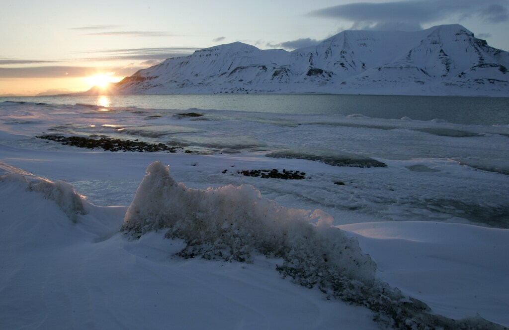the sun shines low in the sky just after midnight over a frozen coastline near the Norwegian Arctic town of Longyearbyen