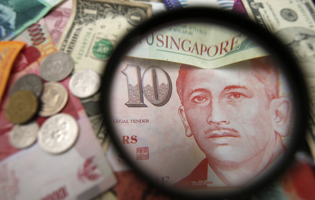 Singapore currency notes are seen through a magnifying glass among other currencies in this photo illustration taken in Singapore April 12, 2013. Singapore on Friday held monetary policy steady as expected and said it will maintain the Singapore dollar's "modest and gradual" appreciation path as it expects economic growth to pick up gradually over the course of the year. REUTERS/Edgar Su (SINGAPORE - Tags: BUSINESS)