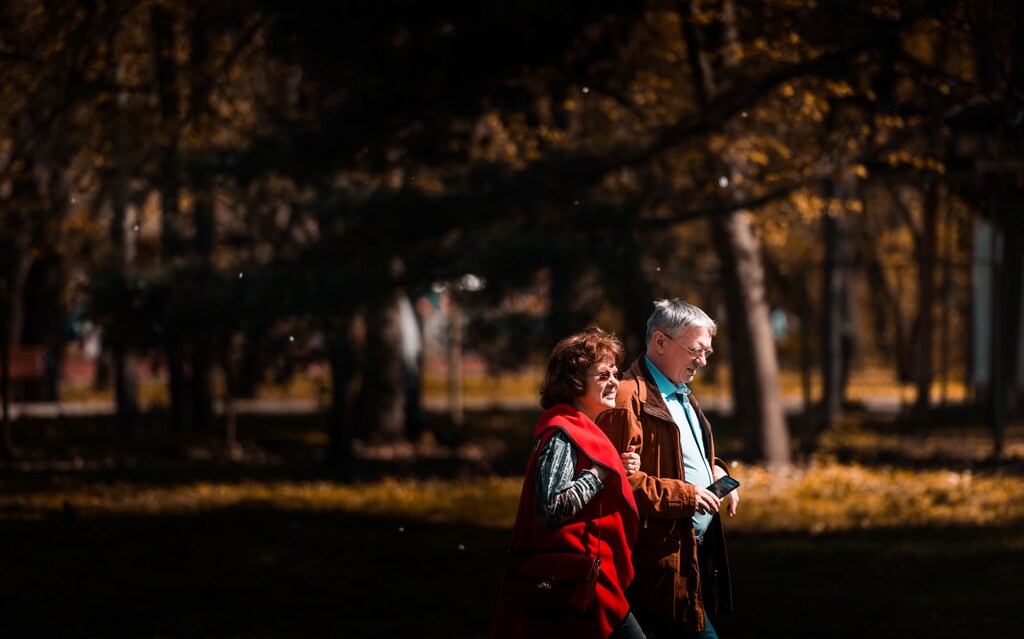An older couple walking arm in arm through a wooded area