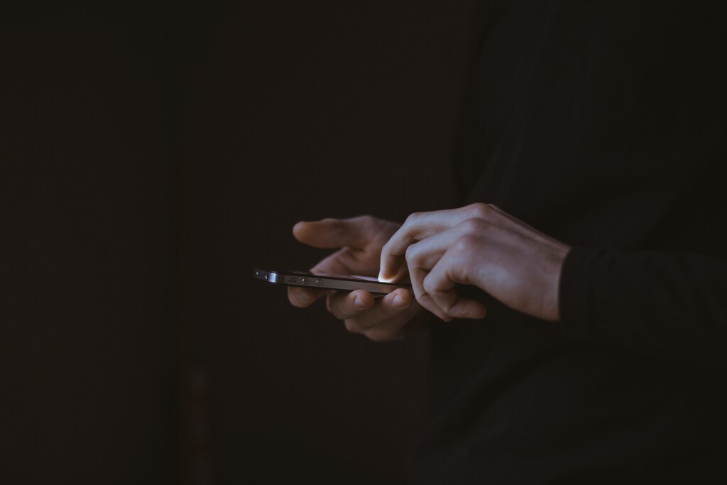 What do we need to consider for Central Bank Digital Currencies to be implemented successfully? Pictured: Two hands holding a mobile phone in darkness.