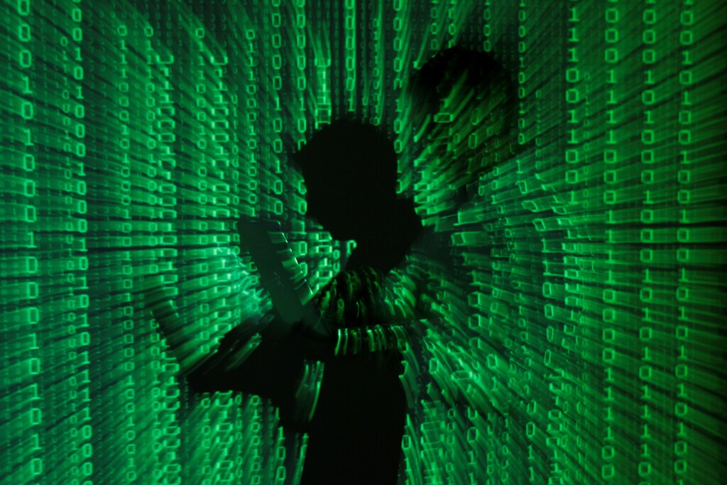 An illustration picture shows a projection of binary code on a man holding a laptop computer, in an office in Warsaw.