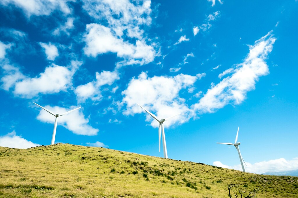 Three wind turbines on a hill against a blue sky: There is a $1.7 trillion investment need in clean energy in the Global South