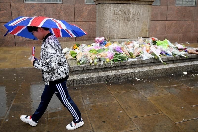 A pedestrian carrying an umbrella walks past floral tributes to the victims of the recent attack at London Bridge and Borough Market, in central London, Britain June 6, 2017. REUTERS/Toby Melville - RTX39894