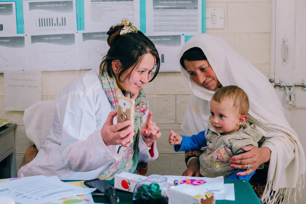 Una profesional sanitaria muestra a una madre y su hijo un teléfono en un centro de salud en el norte de Pakistán.