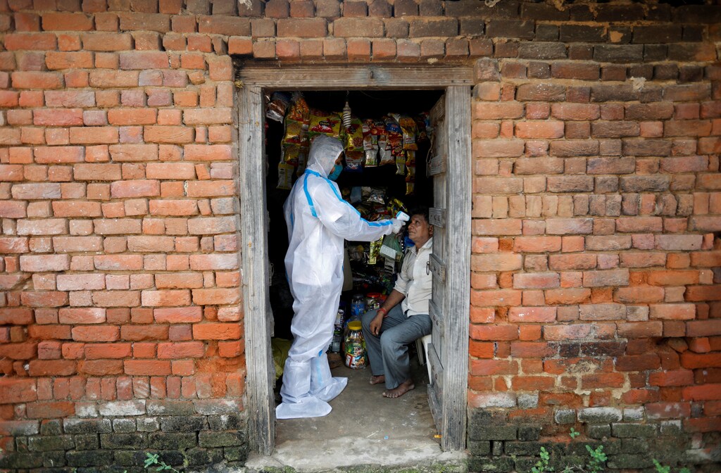 A healthcare worker wearing personal protective equipment (PPE) checks the temperature of a man inside his shop during a door-to-door survey for the coronavirus disease (COVID-19), in Dehgamda village in the western state of Gujarat, India, September 21, 2020