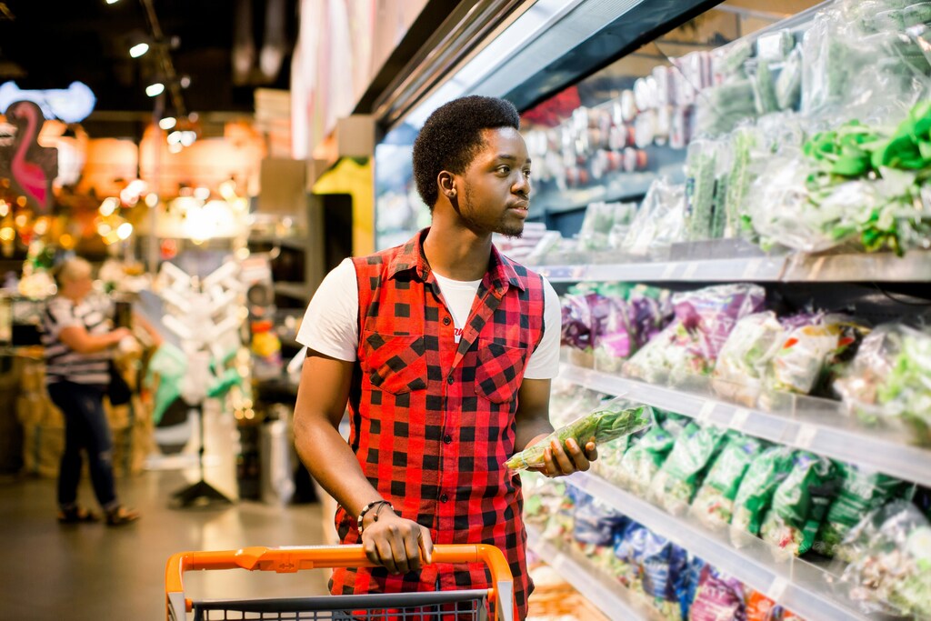 Man in red and black checkered sleeveless shirt and white t-shirt shopping in salad section of supermarket: Consumers may be willing to pay a bit more for sustainable products, so why don't they?